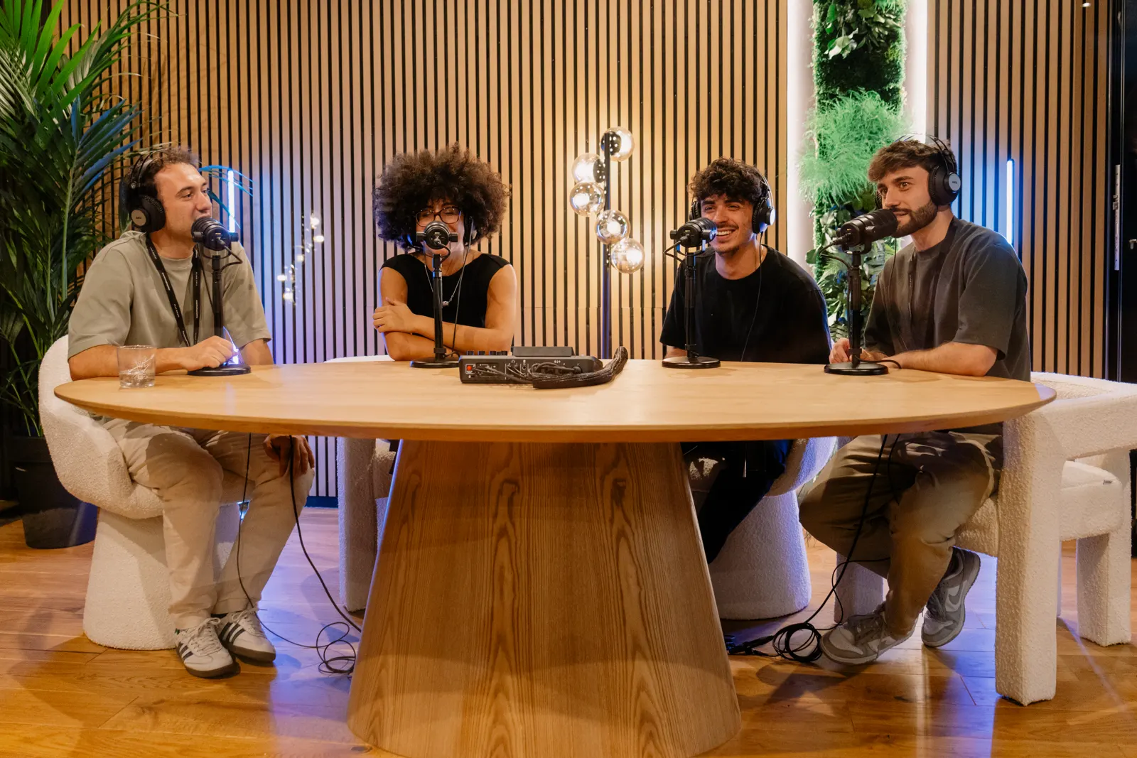 Four people recording a podcast around a round wooden table in the Feat.House studio